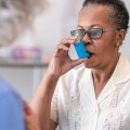 A senior black women with asthma is learning how to use an inhaler. The female doctor is showing her how to use the asthma inhaler.